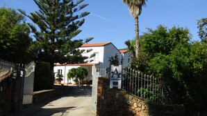 A gated entrance to a building with a stone wall and a metal gate, surrounded by trees and potted plants.