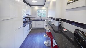 Une cuisine moderne avec des meubles blancs, un plan de travail noir et des tabourets de bar rouges.