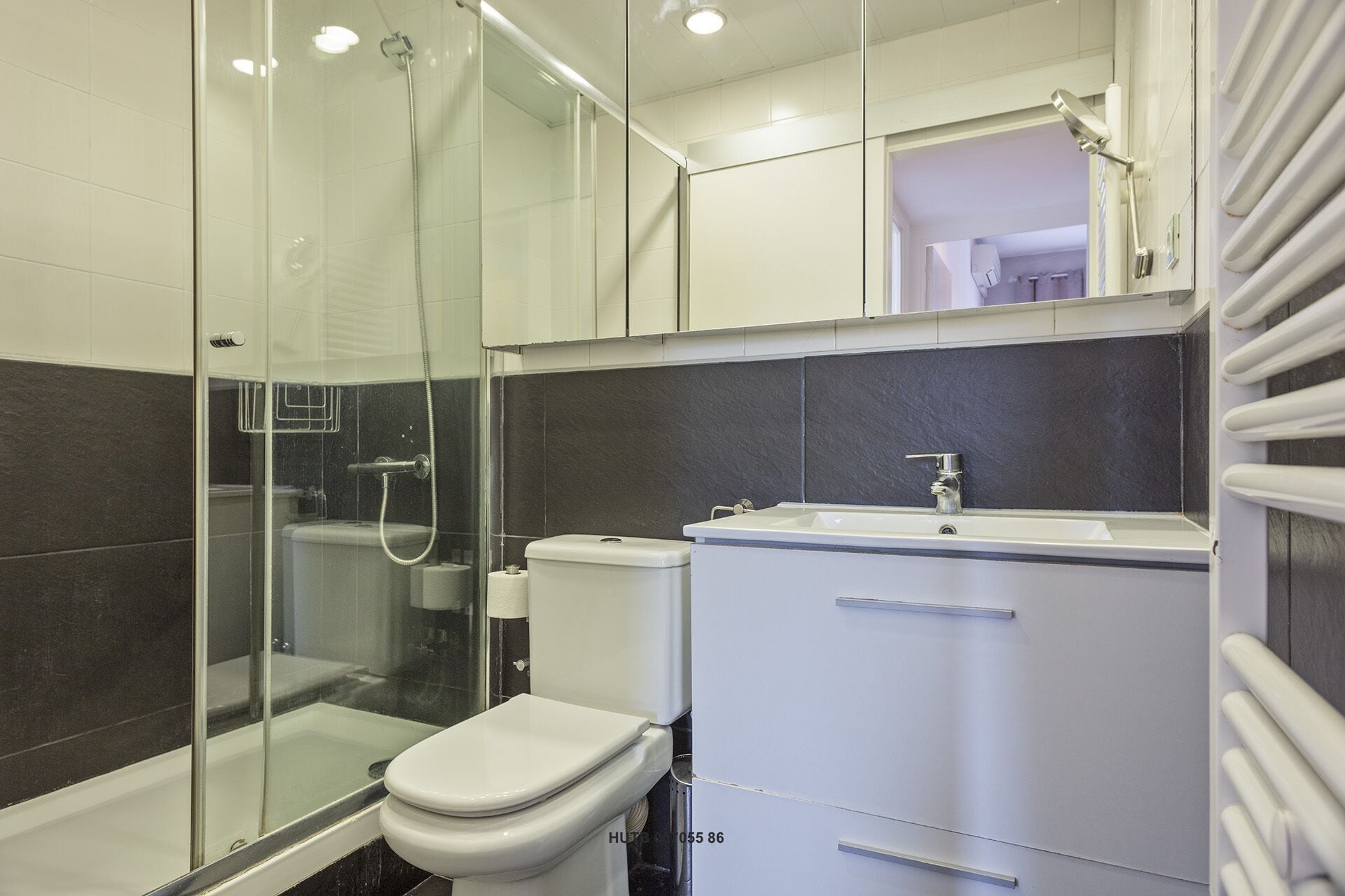 Een moderne badkamer met een douchecabine van glas, een wit toilet en een wastafel met een spiegel erboven.