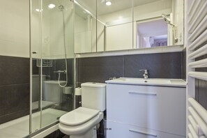 Ein modernes Badezimmer mit einer Glaskabine zur Dusche, einer weißen Toilette und einem Waschbecken mit Spiegel darüber.