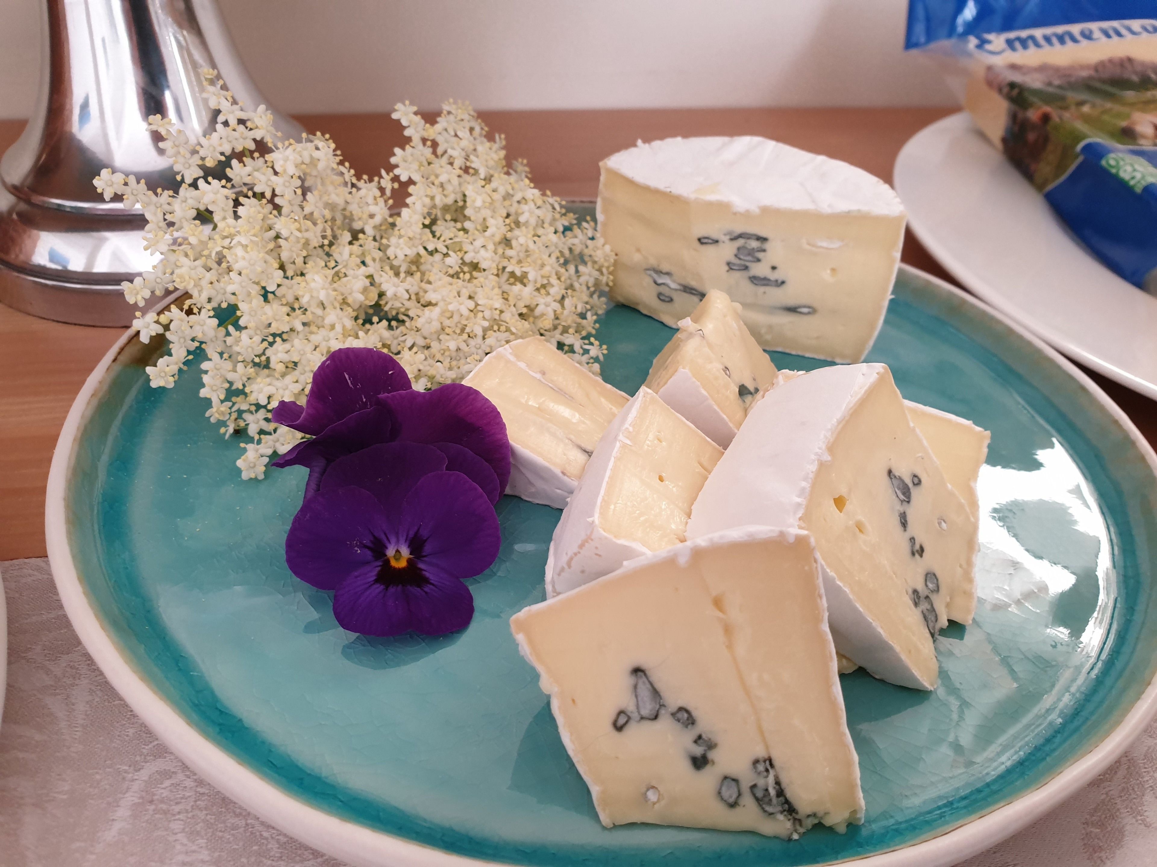 A plate with various cheeses and flowers on a teal plate.