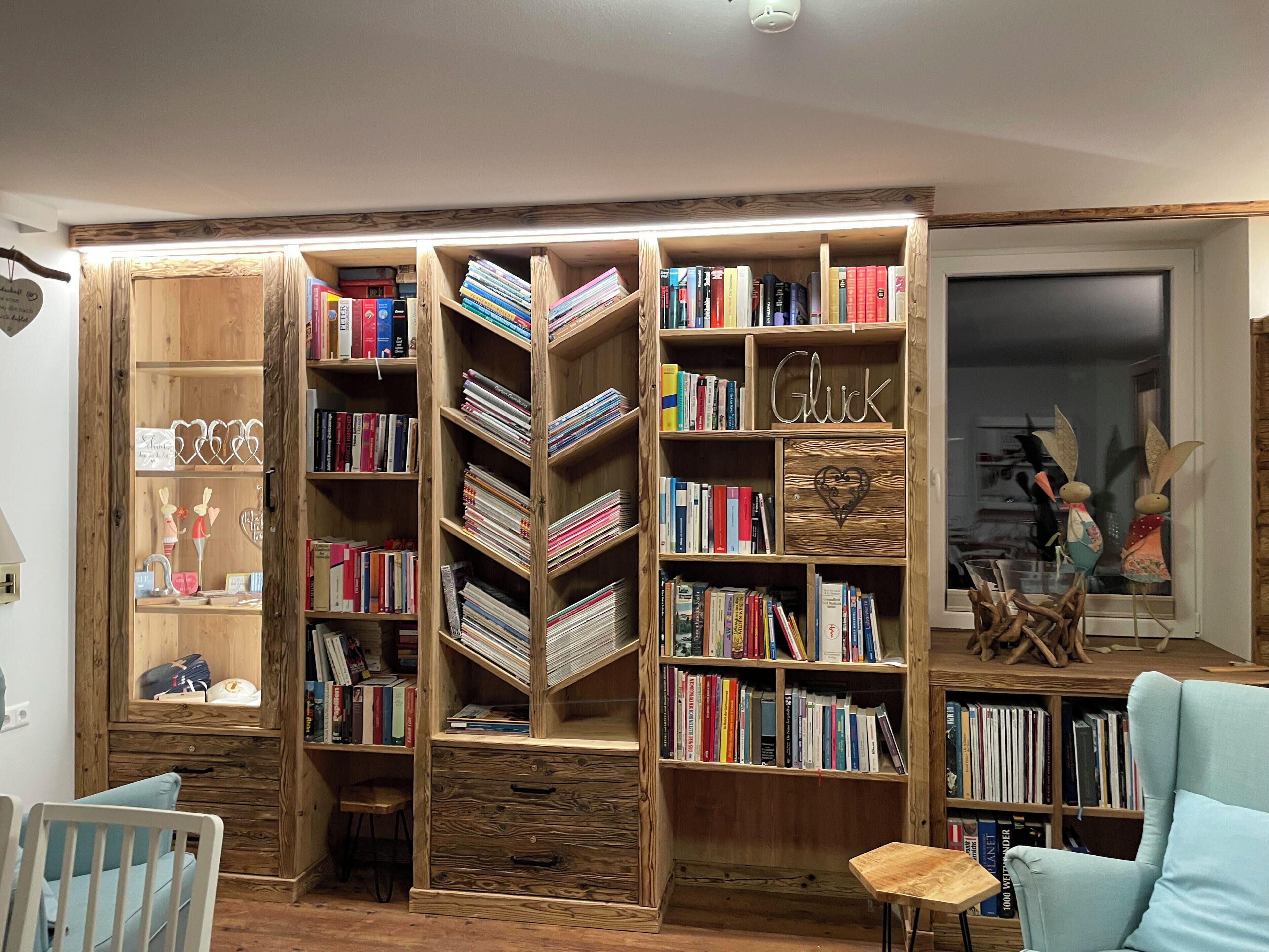 A room with a large wooden bookshelf filled with books, a small wooden desk, and a light blue armchair.