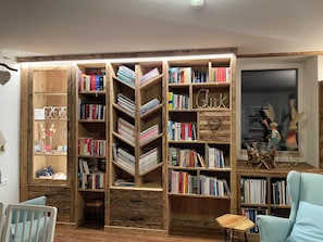 A room with a large wooden bookshelf filled with books, a small wooden desk, and a light blue armchair. - Bed & Breakfast Mittelkärnten (Althofen)