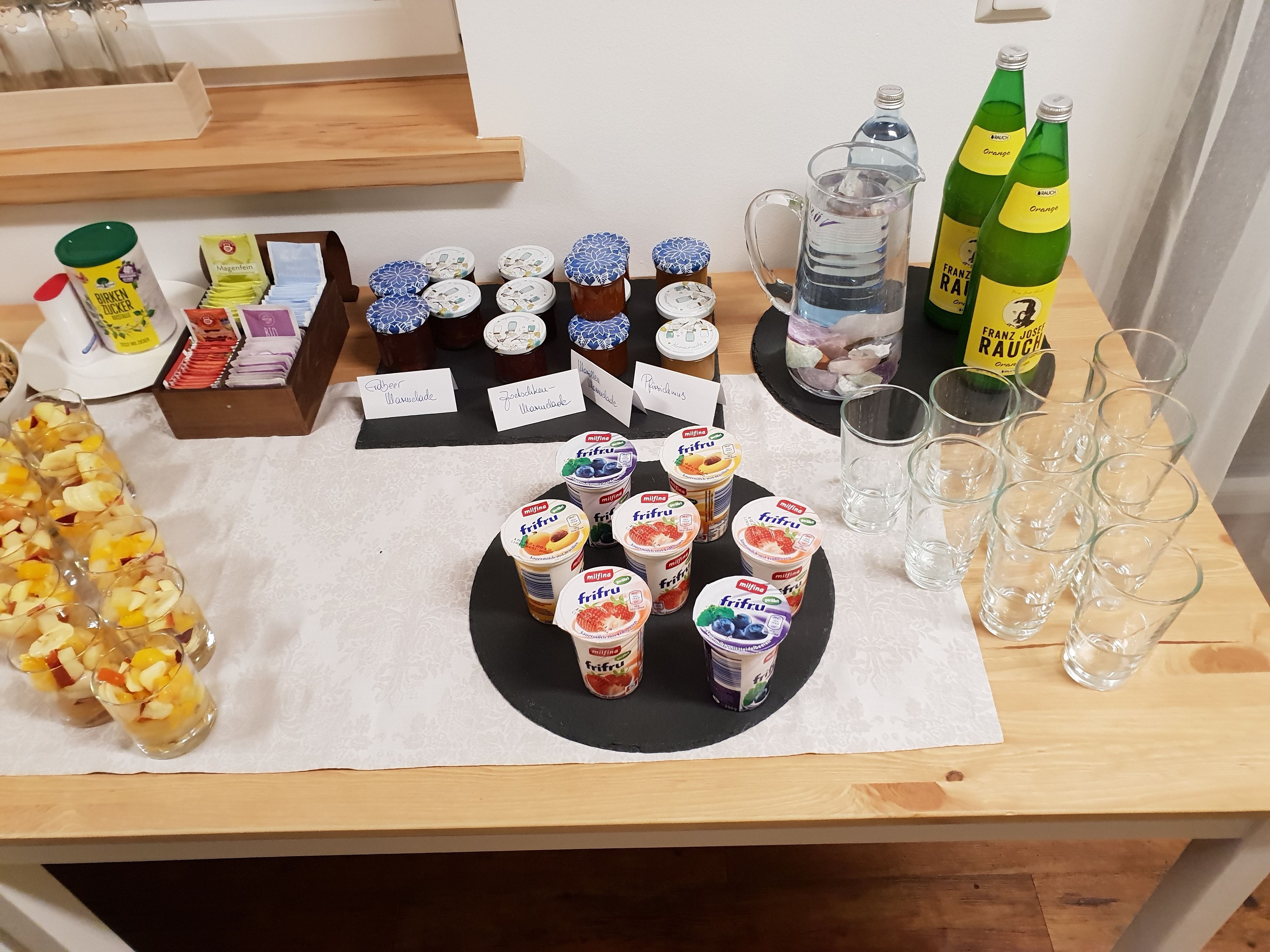 A table with various food items, including fruit cups, yogurt, and bottles of orange juice.