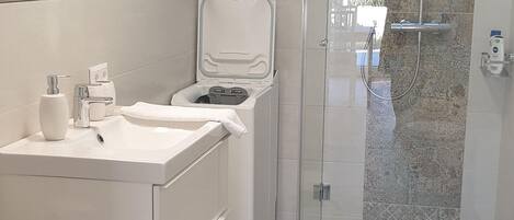Un baño moderno con cabina de ducha de vidrio, lavamanos blanco y espejo sobre él.