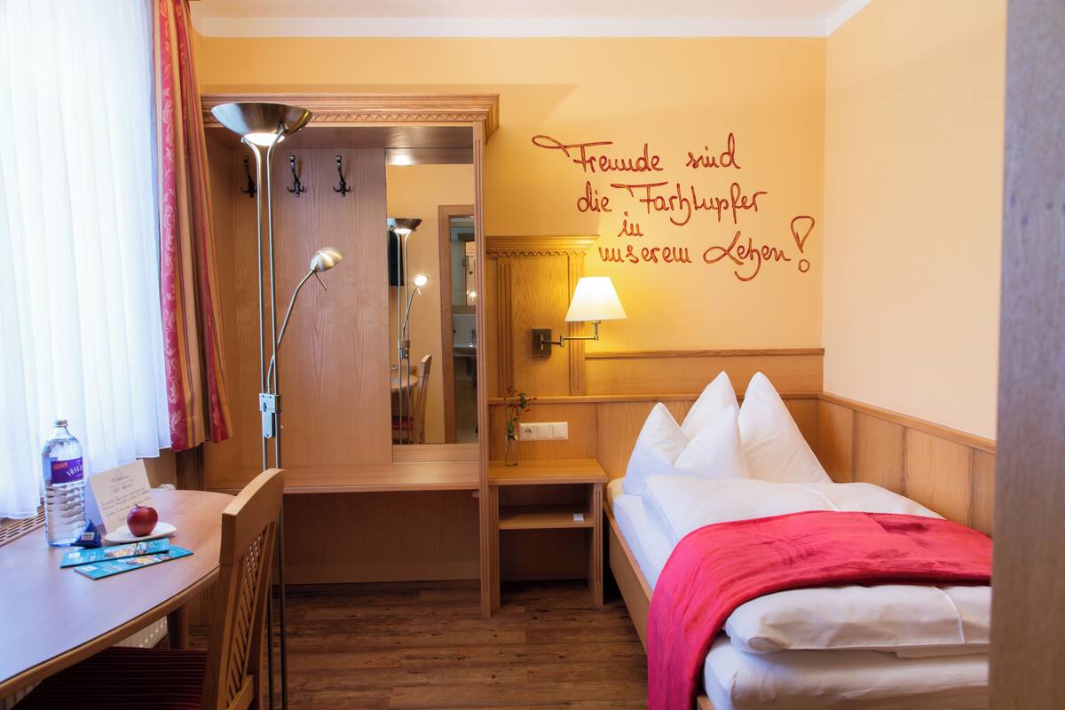A hotel room with a bed, bedside table, lamp, and a mirror.