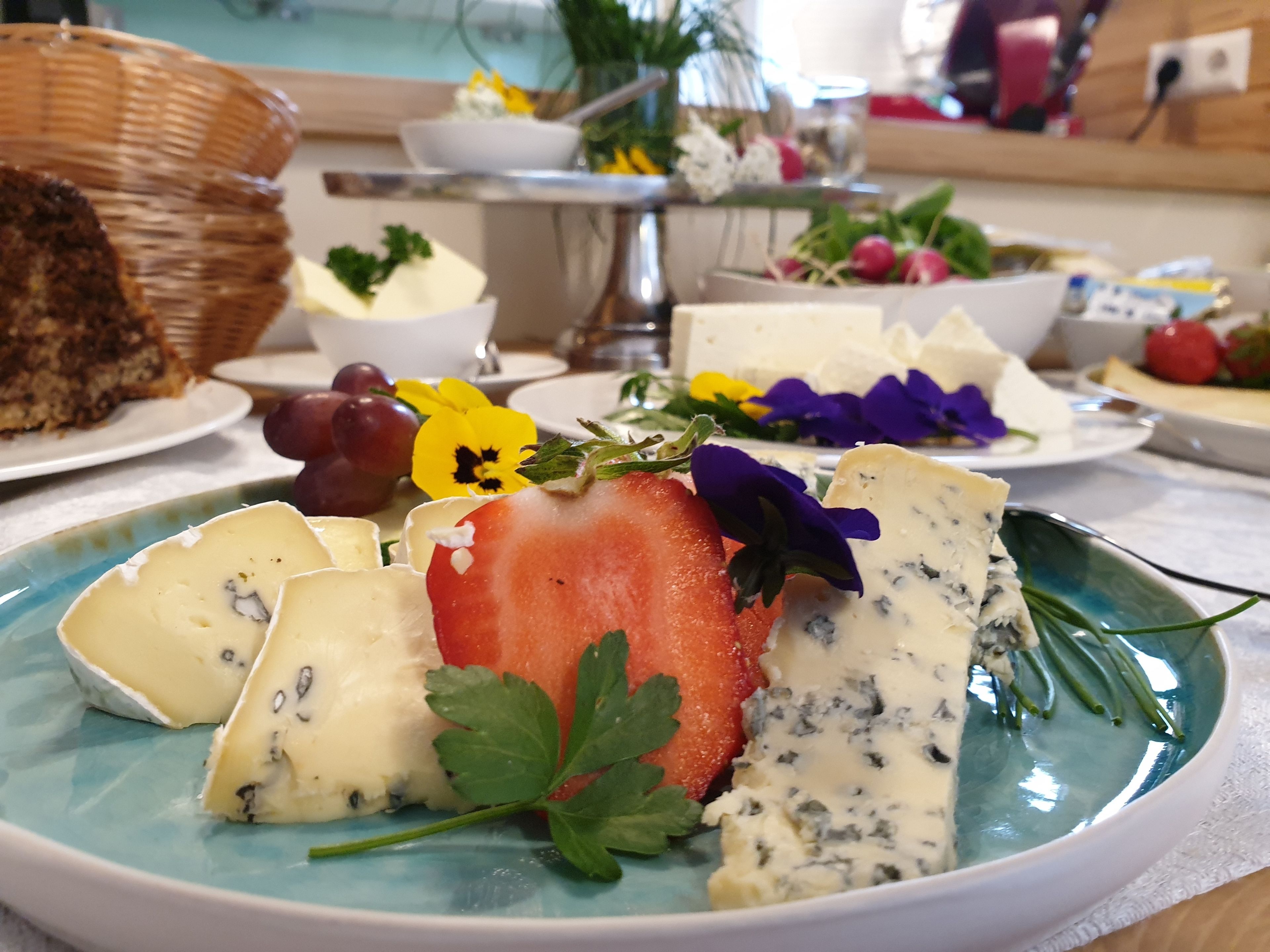 Un plat amb formatges variats, una maduixa i flors sobre una taula.