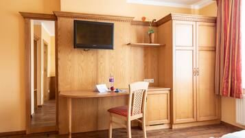 A hotel room with a wooden desk, a chair, a television, a wardrobe, and a mirror.