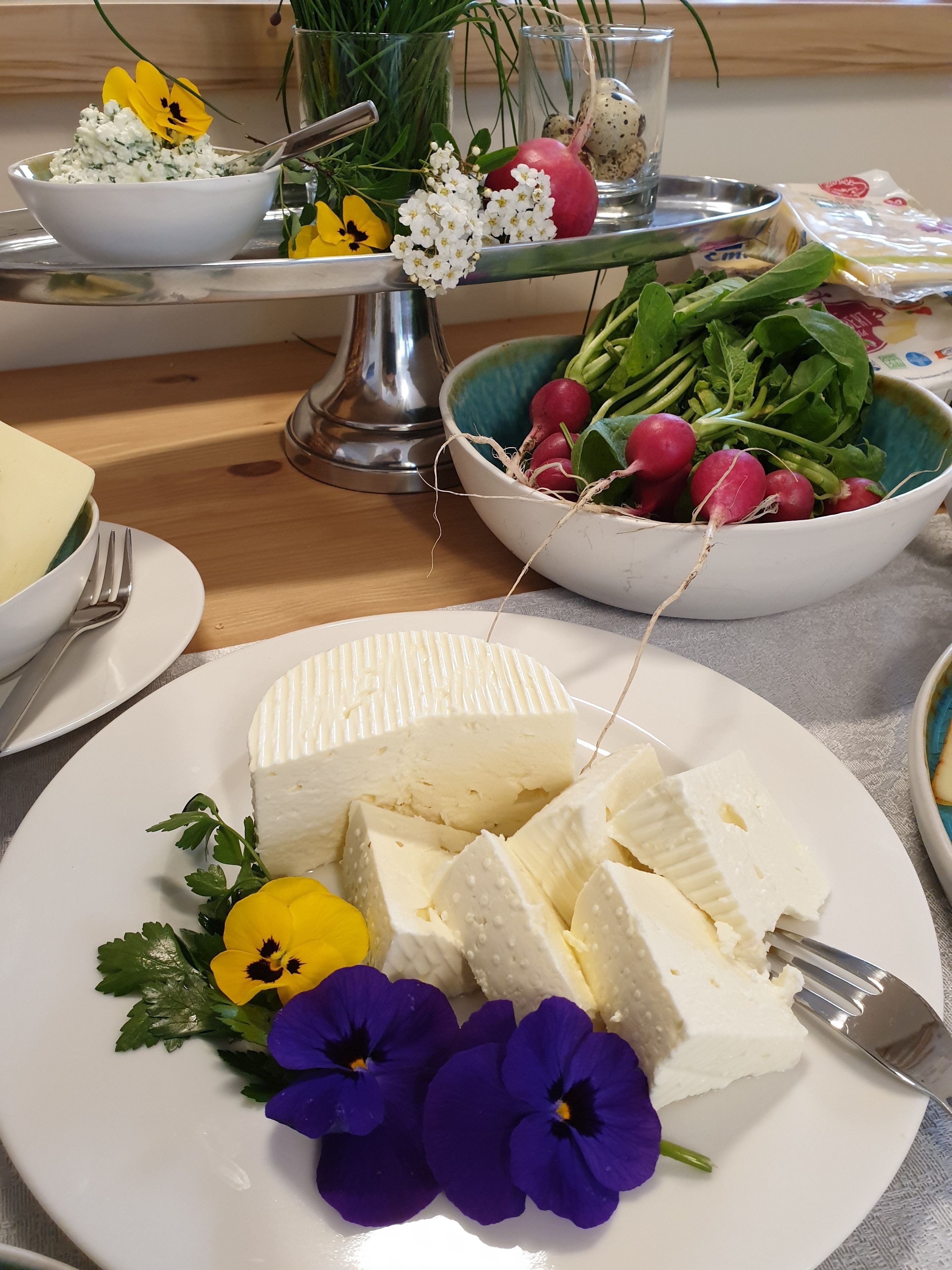 Ein Käseplatte mit Blumen und eine Schale Radieschen.