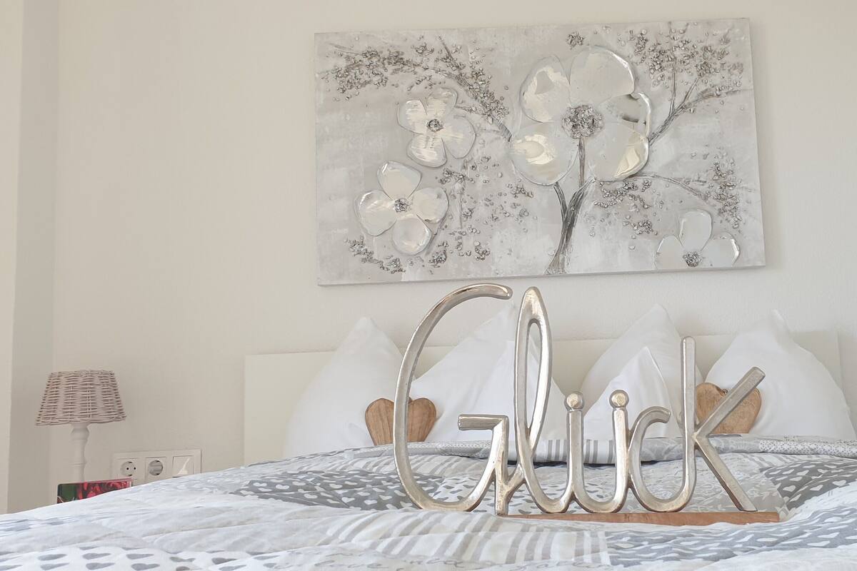 A neatly made bed with a patterned bedspread, a decorative wall piece above, and a bedside table with a lamp.