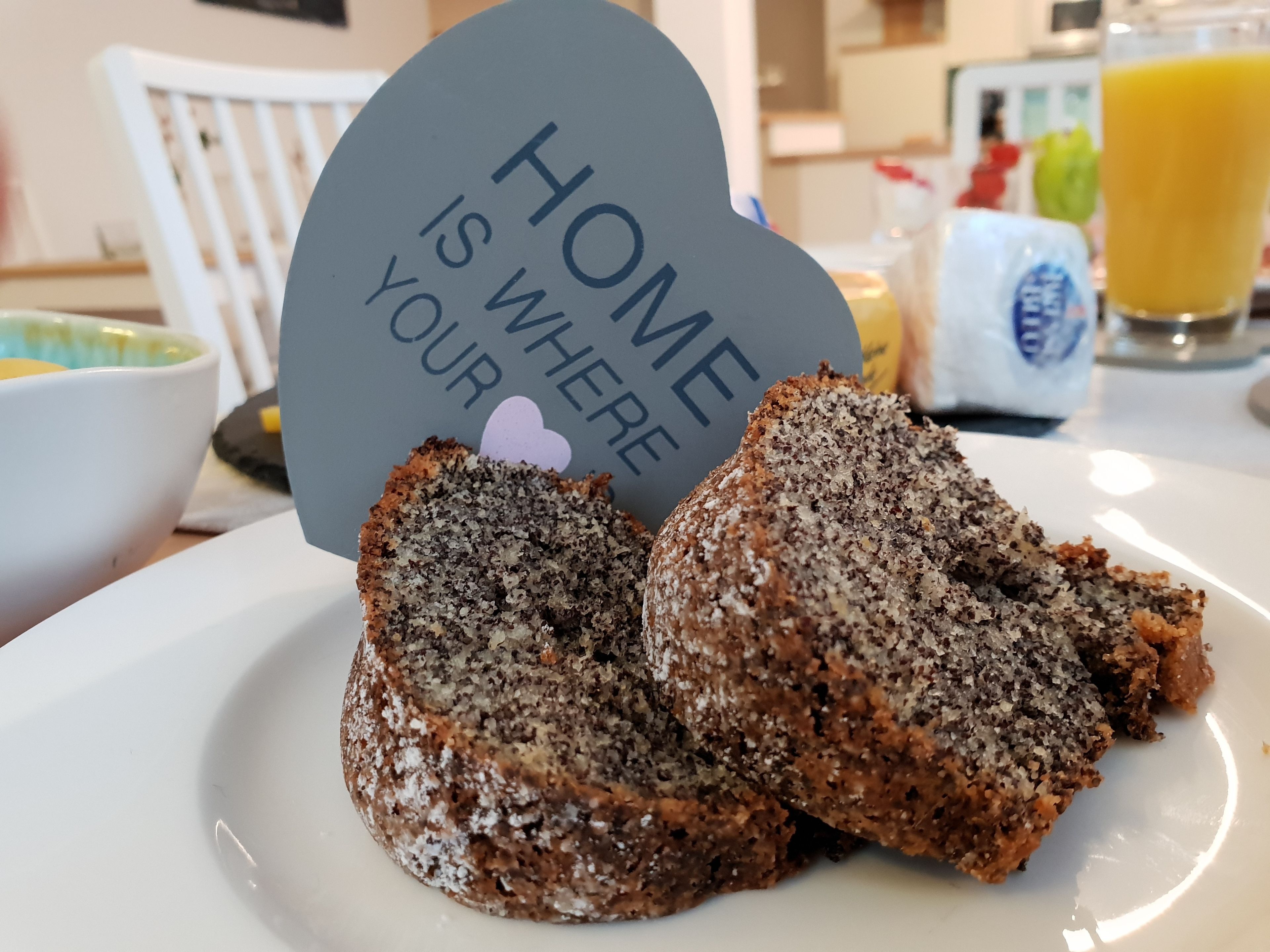 Um prato com dois pedaços de bolo de sementes de papoula e um letreiro que diz 'O lar é onde está o seu coração'.