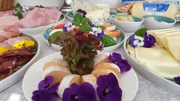 A table with various food items including meats, cheeses, and vegetables, arranged on plates with decorative flowers.