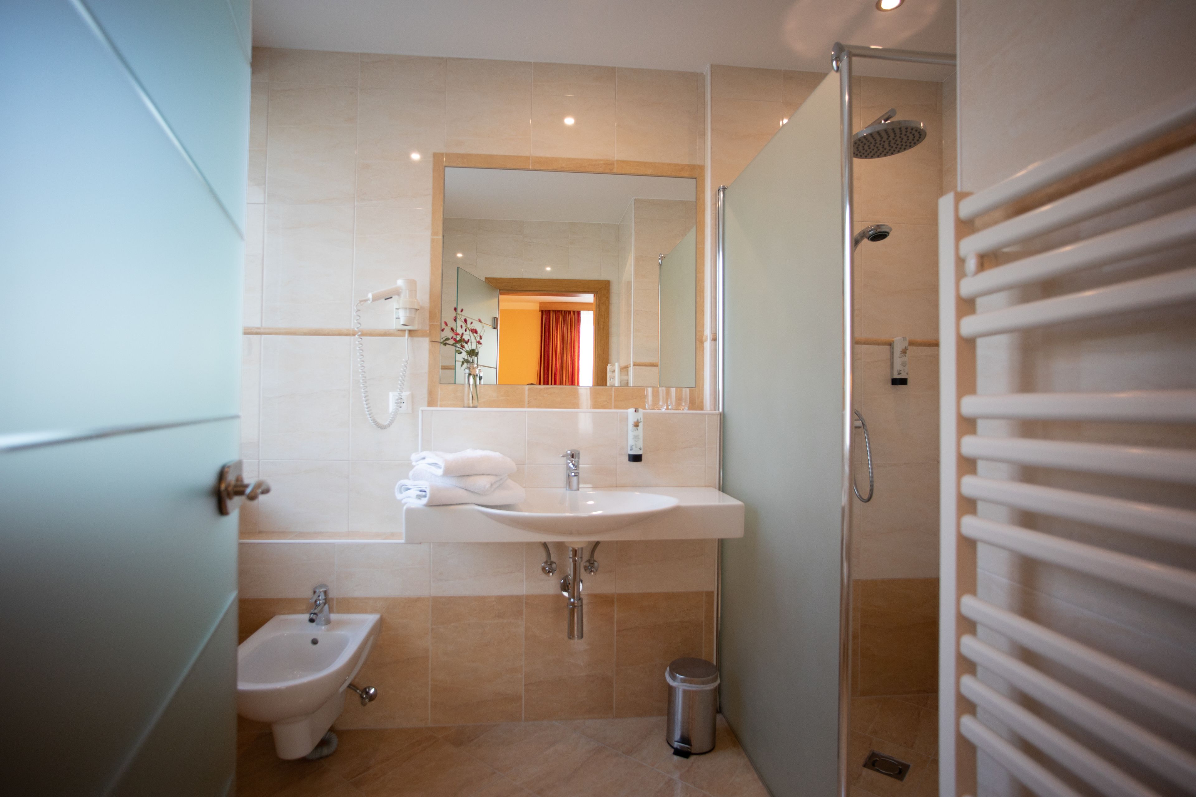 A modern bathroom with a sink, bidet, mirror, and shower.