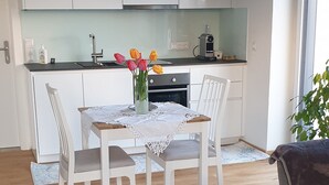 A modern kitchen with white cabinets, a dining table with chairs, a coffee machine, and a vase with flowers. - Bed & Breakfast Mittelkärnten (Althofen)