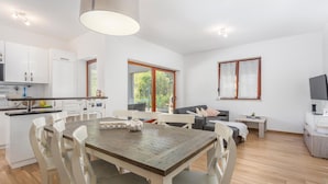 A modern kitchen with white cabinets, a dining table with chairs, a sofa, and a TV. - Gorgeous home in Gostinjac (Gostinjac)