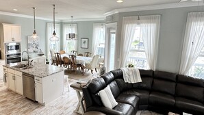 Een moderne keuken met een centraal eiland, een eethoek met een tafel en stoelen, een zwarte leren bank en een kleine ronde tafel.