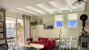 A living room with a red sofa, a black leather couch, a white coffee table, and a clear glass table. There is a black heater on the wall and a window with a view of the sky. - comfortable house in Lacanau Ocean, everything in walking distance (Lacanau)
