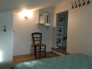 Ein Schlafzimmer mit einem Bett, einem Sessel, einem Spiegel und einem Kleiderständer.