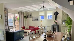 A spacious living area with a red sofa, a dining table with a vase of flowers, and a view of the outside through large windows. - comfortable house in Lacanau Ocean, everything in walking distance (Lacanau)