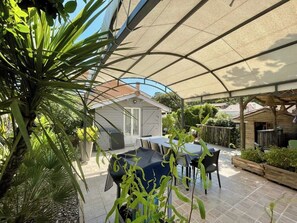 An outdoor patio area with a covered seating area, a pool, and surrounding greenery. - Beautifully furnished house with terraces G0254 (Lacanau)