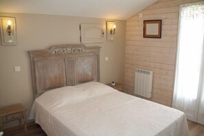 Un dormitori amb un panell de fusta al capçal, una taula de nit, un radiador i una finestra amb cortines.
