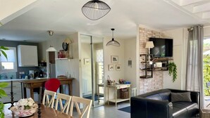 A modern living room with a black leather sofa, a dining table with chairs, a kitchen area, and a TV mounted on a brick wall. - comfortable house in Lacanau Ocean, everything in walking distance (Lacanau)