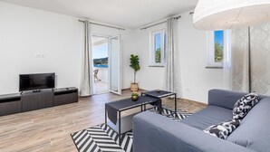 Een moderne woonkamer met een flatscreen televisie, een bank, een salontafel en uitzicht op een balkon met een zwembad.