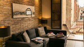 A cozy living room with a brick wall, a modern sofa, a lamp, and a view of the city through a large window. - Alcam Molino (Barcelona)