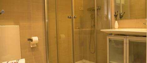 A glass-enclosed shower with a handheld showerhead, a white towel, and a small gift bag on the floor.