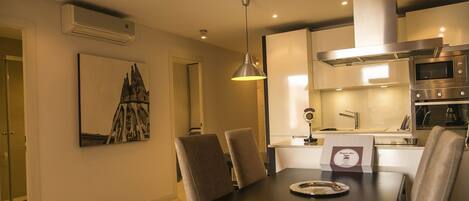 Una cocina moderna con electrodomésticos de acero inoxidable, un comedor con mesa y sillas, e iluminación colgante.