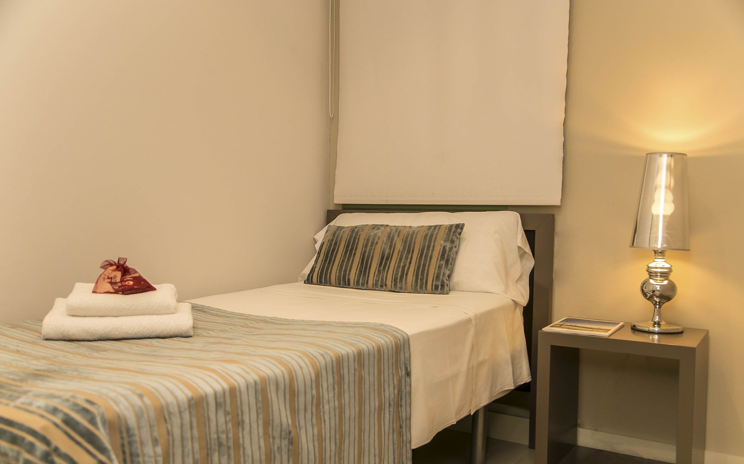 A hotel room with a bed, a nightstand with a lamp, and a wall-mounted TV.