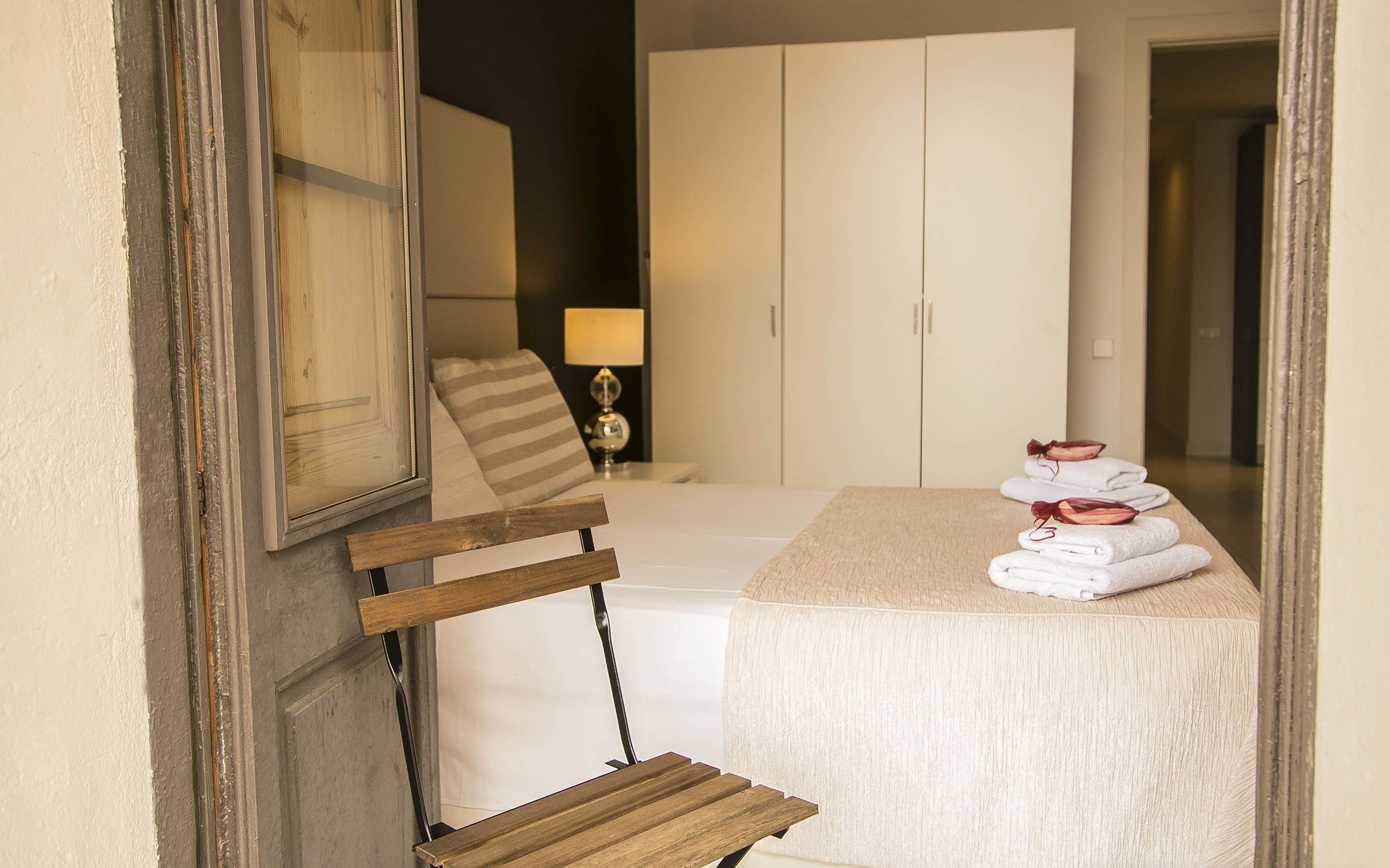 A hotel room with a bed, a wooden chair, a table with towels, and a lamp.