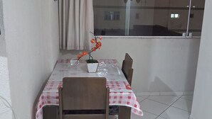 A dining area with a table covered by a checkered tablecloth, two chairs, and a potted plant. - BUILDING FACING THE SEA IN PRAIA GRANDE-SP (Guilhermina)