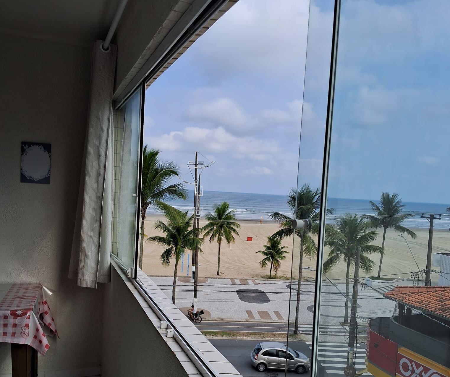 A view from a window overlooking a beach with palm trees, a road, and a car.