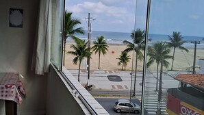 A view from a window overlooking a beach with palm trees, a road, and a car. - BUILDING FACING THE SEA IN PRAIA GRANDE-SP (Guilhermina)
