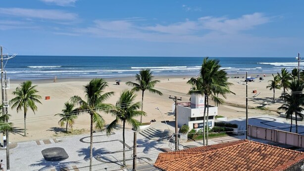 A beach view with palm trees, a sandy beach, and a clear blue sky. - BUILDING FACING THE SEA IN PRAIA GRANDE-SP (Guilhermina)