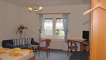 A bedroom with a bed, a desk, two chairs, a television, and a window with curtains.