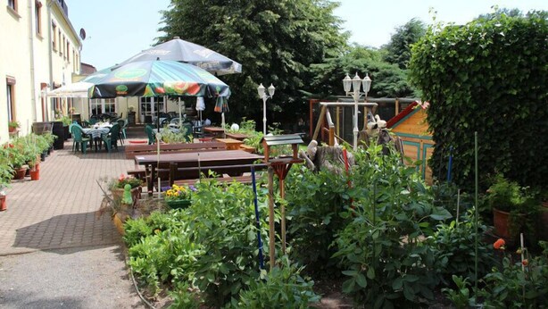 An outdoor patio with tables and chairs, surrounded by potted plants and a garden area. - Hotel Parkschänke Zabeltitz (Grossenhain)