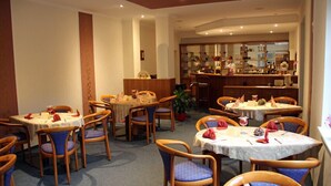 A restaurant with round tables and chairs, a bar area, and a potted plant. - Hotel Parkschänke Zabeltitz (Grossenhain)