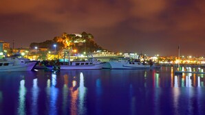 A marina at night with boats docked, a hill with lights, and buildings in the background. - Nice and complete apartment in playa oliva / denia (El Verger)