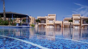 A swimming pool with blue mosaic tiles, surrounded by buildings with beige facades and flat roofs. - Nice and complete apartment in playa oliva / denia (El Verger)