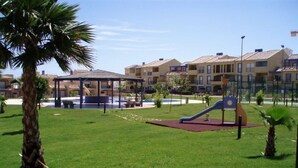 A playground with a slide and a covered seating area, surrounded by well-maintained grass and palm trees. - Nice and complete apartment in playa oliva / denia (El Verger)