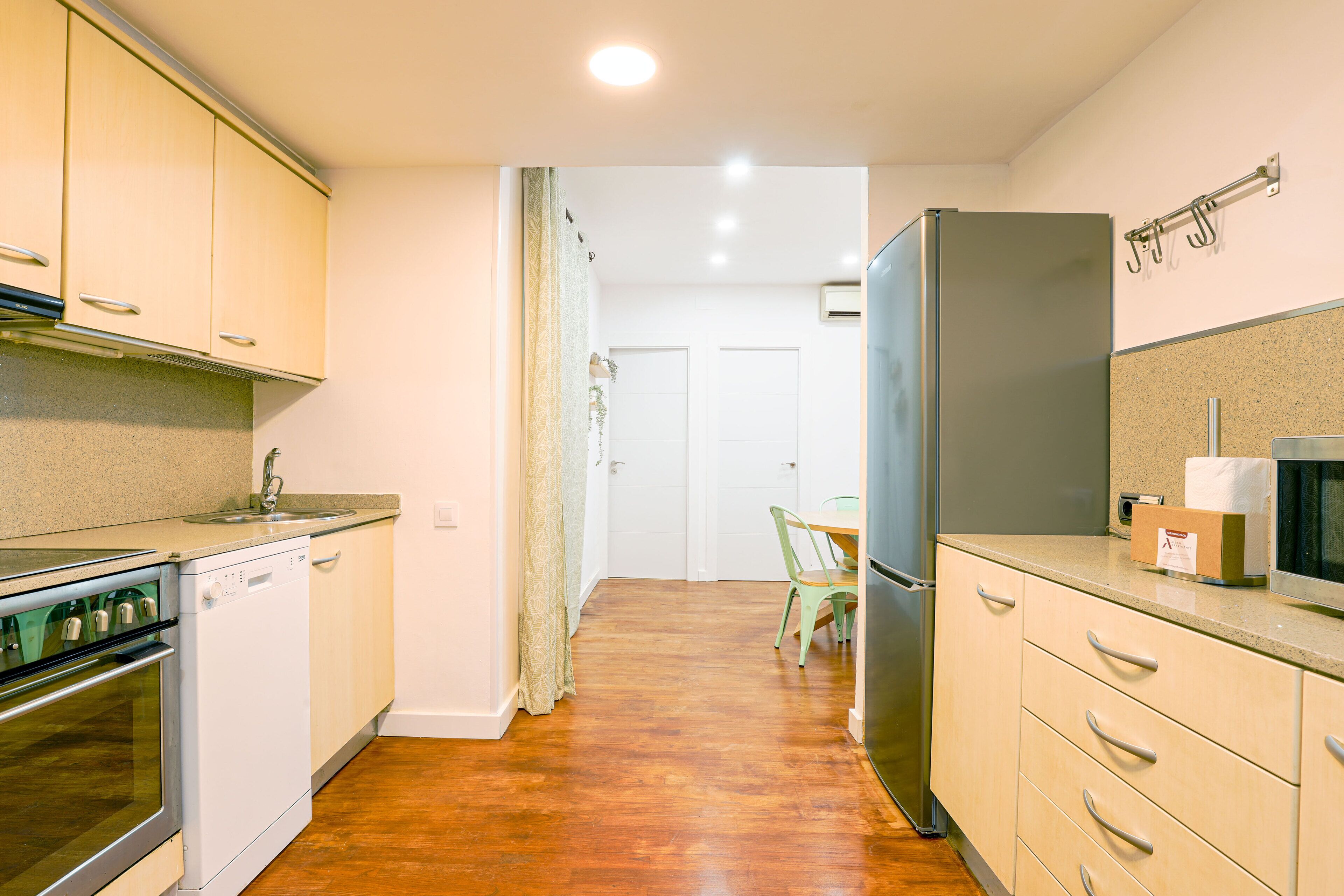 A compact kitchen with a dishwasher, oven, refrigerator, and a small dining area with a chair.