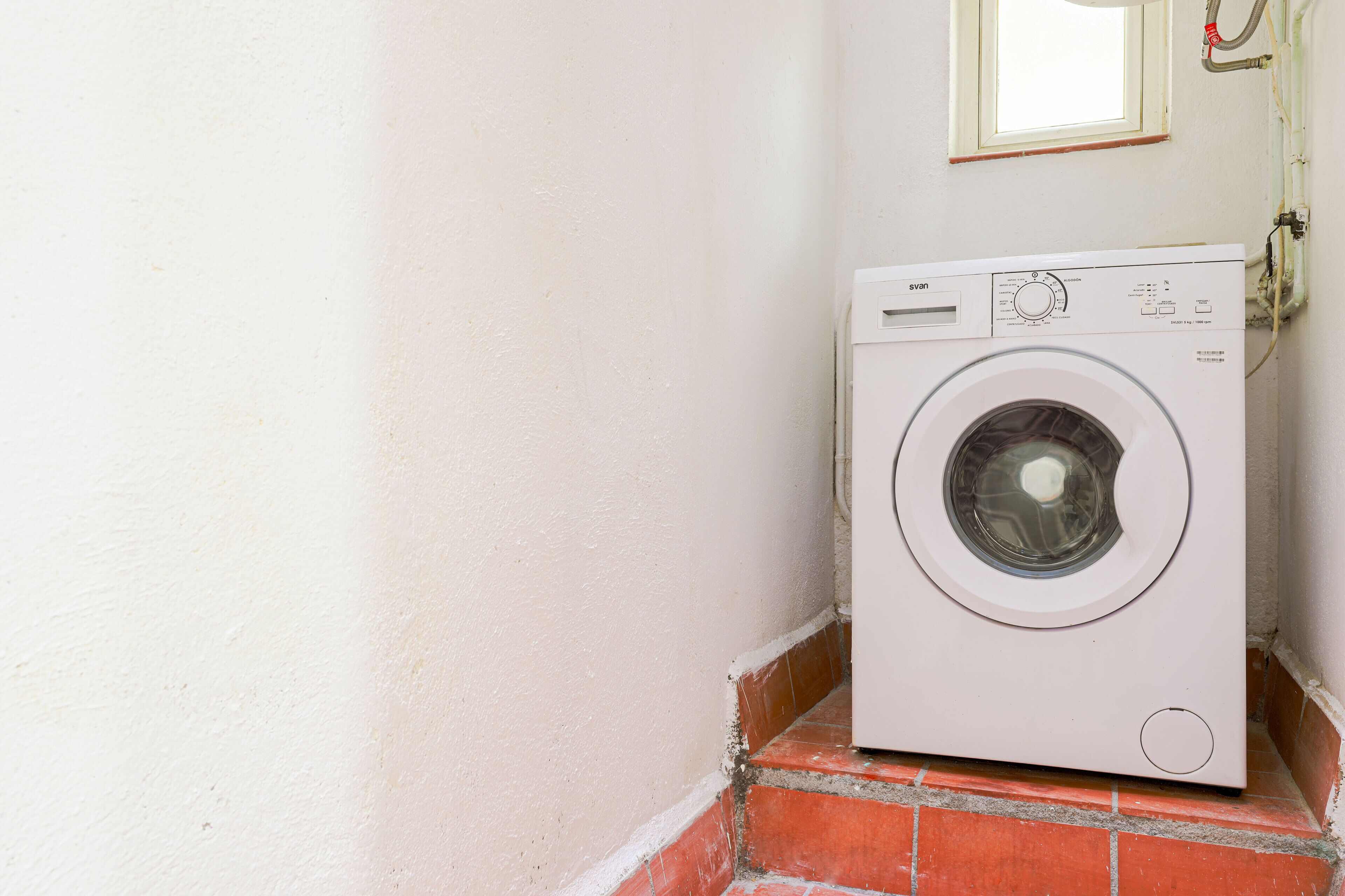 A white washing machine in a corner with a window above it.