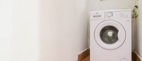 A white washing machine in a corner with a window above it.