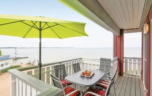 A balcony with a table and chairs, a green umbrella, and a view of the water. - Cozy apartment in Rechlin with sauna (Rechlin)