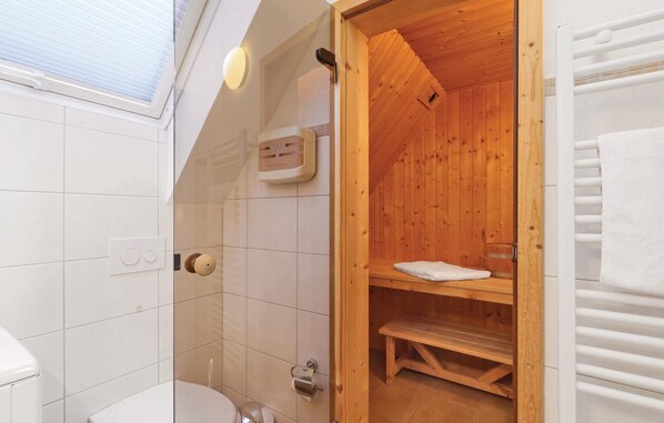 A wooden sauna with a bench and a towel, a toilet, and a window with blinds. - Cozy apartment in Rechlin with sauna (Rechlin)