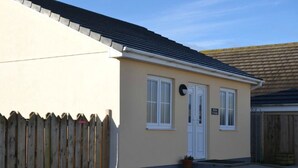 A single-story building with a beige exterior, white trim, and a dark roof. There is a wooden fence in front, and a small potted plant on the steps leading to the entrance. - Perfect location for exploring the local 7 bays, Wifi, local amenities (Padstow)