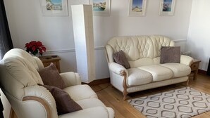 A living room with two cream-colored leather sofas, a patterned rug, and framed artwork on the walls. - Perfect location for exploring the local 7 bays, Wifi, local amenities (Padstow)