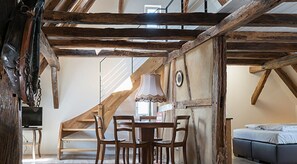 A rustic room with exposed wooden beams, a dining table with chairs, a lamp, and a bed. - Pension Pauserei (Oedheim)